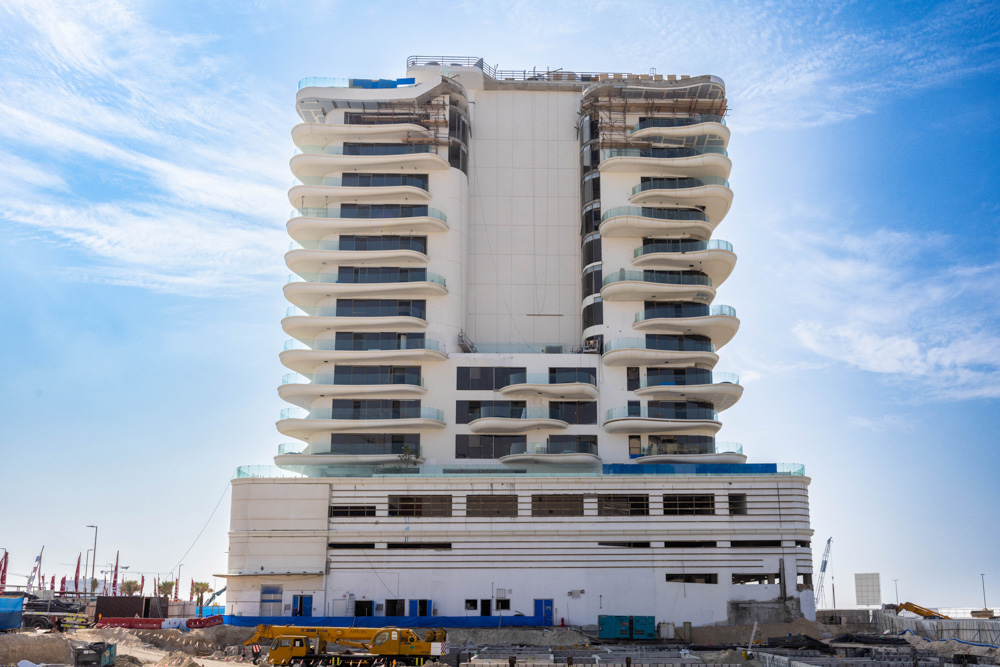 Beach Walk Residence A modern multi-story building under construction with balconies, surrounded by a construction site and blue sky.